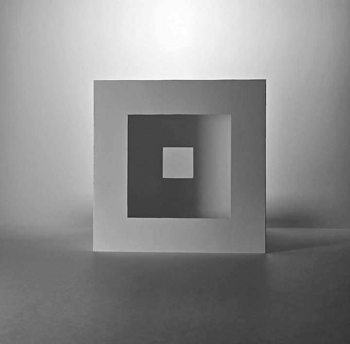 A black and white concept created with lighting that accentuates the lines and layers of a cube. Cut through the middle is different sized square holes creating an illusion of depth in layering.